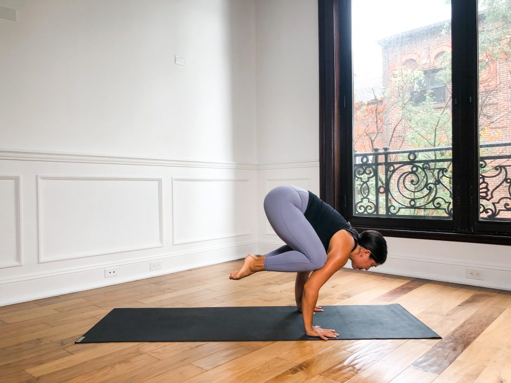 girl in crow pose on a yoga mat, knees resting on the back of the elbows