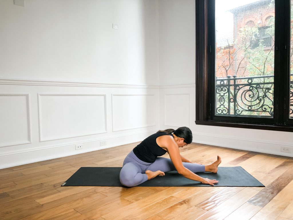 Yogi on a black yoga mat in Head to Knee Pose (Janu Sirsasana)