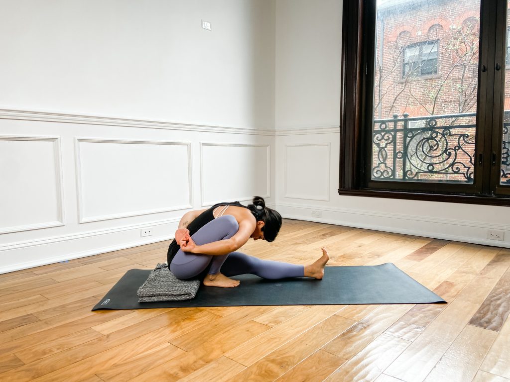 Person doing Marichyasana I on a yoga mat with a blanket beneath their sitting bones