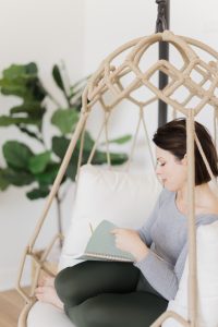 Jordan Ashley of Souljorn Yoga sitting in a hanging chair, journaling about yoga retreats